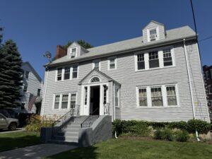 grey 2-family home with center stairs on the outside and front lawn.
