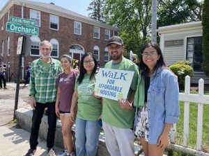 People standing by HCA's building at Orchard Place holding a walk for affordable housing sign