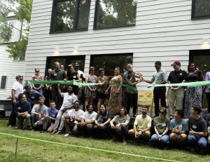 crowd holds green ribbon in front of housing unit as two people cut the ribbon