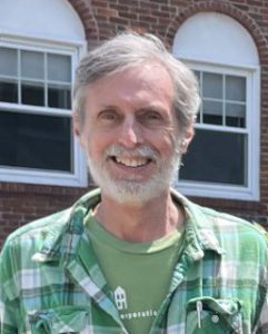 white man with greying hair and beard smiling, wearing green shirt