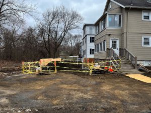 2-family home with dirt in rear and safety tape around area of dirt and trenching