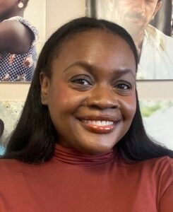 Head shot of Black woman in burnt orange top and long black hair smiling into the camera