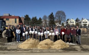 Large group in front of construction site and behind piles of dirt with shovels and hard hats