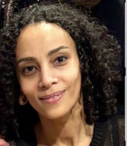 Close up of black woman with tight curly hair, tilting her head and smiling at the camera